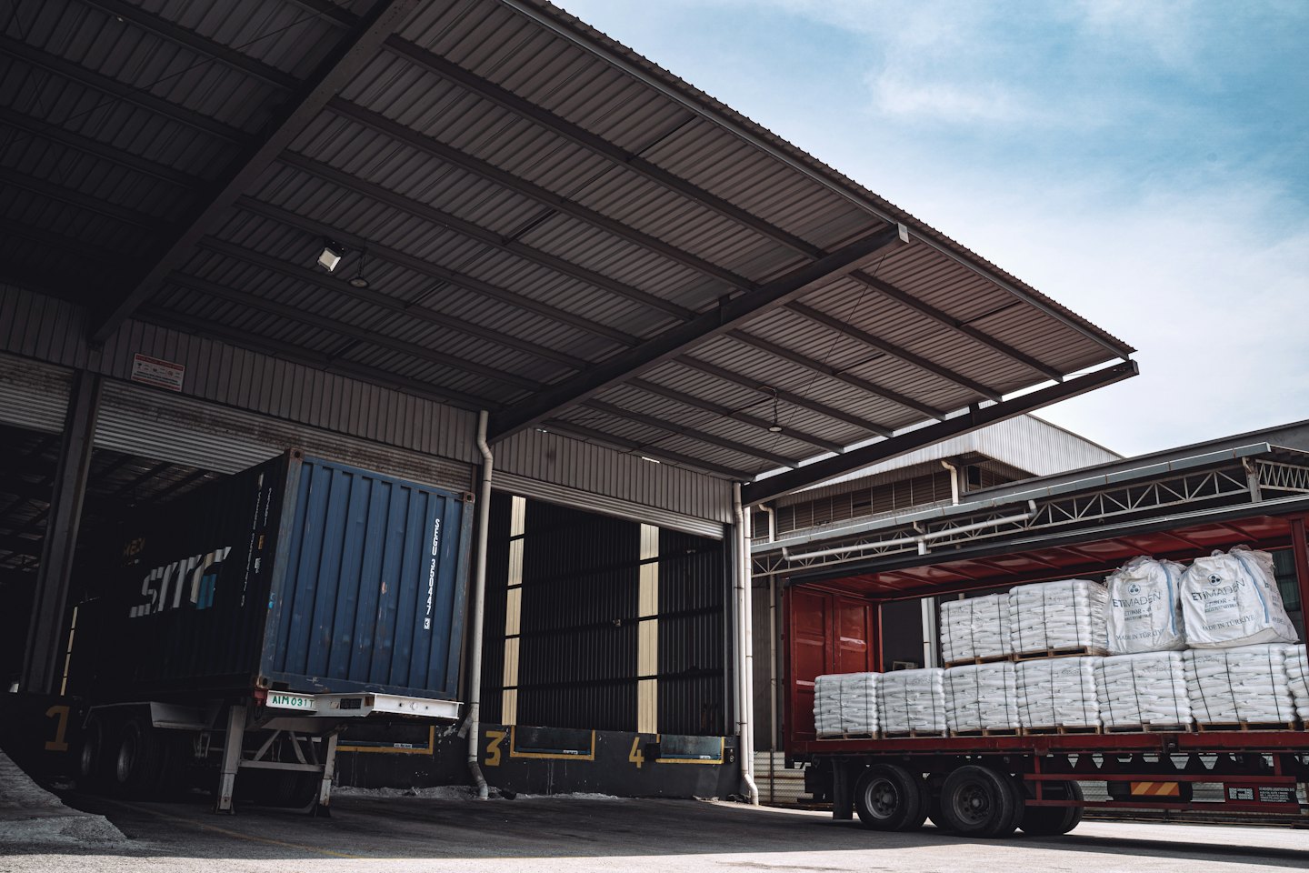 Two trucks parked at warehouse loading bays for shipping.