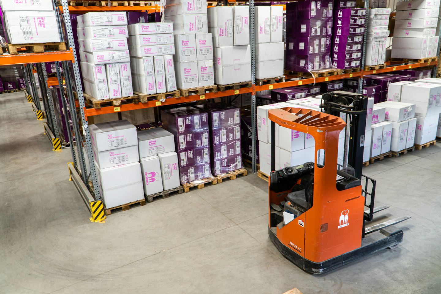Orange forklift parked in a warehouse aisle with stacked boxes.